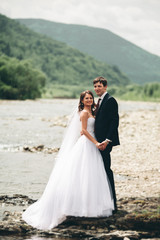 Fototapeta na wymiar Beautifull wedding couple kissing and embracing near the shore of a mountain river with stones 