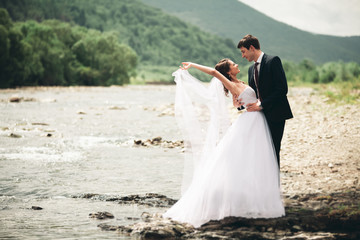 Beautifull wedding couple kissing and embracing near the shore of a mountain river with stones 