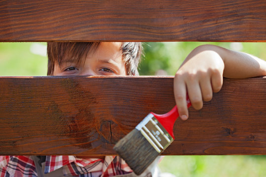 Young boy painting the wooden fence
