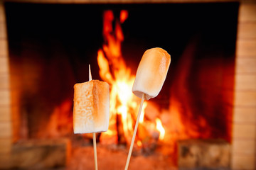 Two marshmallows on sticks being roasted by the fire