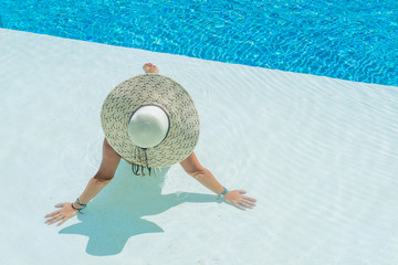 Fototapeta na wymiar Woman sitting in a swimming pool in a sunhat