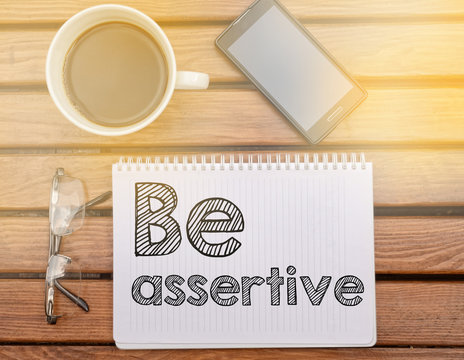Notebook on table with text about soft competence: Be assertive