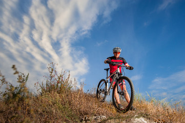 Mountain Bike cyclist resting near his bike in nature on sunny day. Low angle view with cloudy sky on the background. Cross country biking.