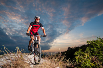Happy man on a mountain bike races downhill in the nature against blue cloudy evening sky. Cyclist...