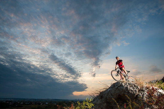 Young cross country biker relaxing on the top of the mountain, enjoying beautiful sunset on overview point.