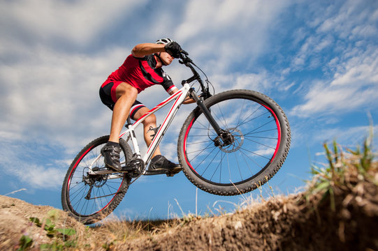 Low angle portrait against blue sky of mountain biker going downhill. Cyclist in red sport equipment and helmet.