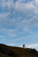 Fototapeta premium cross country cyclist on the top of a hill against cloudy blue sky in the evening