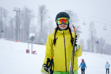 Fototapeta na wymiar Female skier standing with skies in one hand on background beautiful mountain landscape
