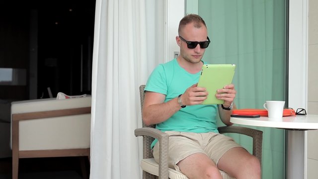 Young man watching pictures from exotic trip on hotel balcony. 