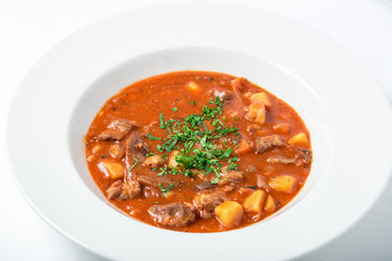 Tomato soup with meat, potatoes, carrots, parsternak in white plate. 