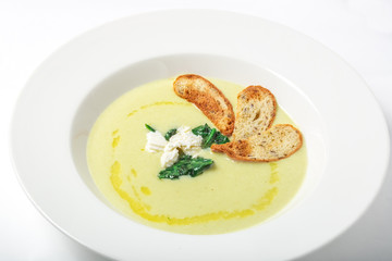 Spinach cream soup with cheese and croutons in white plate.