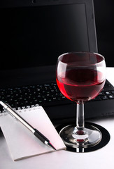 Wineglass, laptop and notebook with pencil
