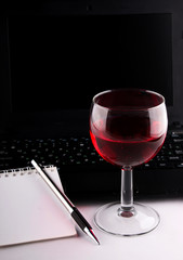 Wineglass, laptop and notebook with pencil