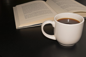 open book with a cup of coffee at the black table