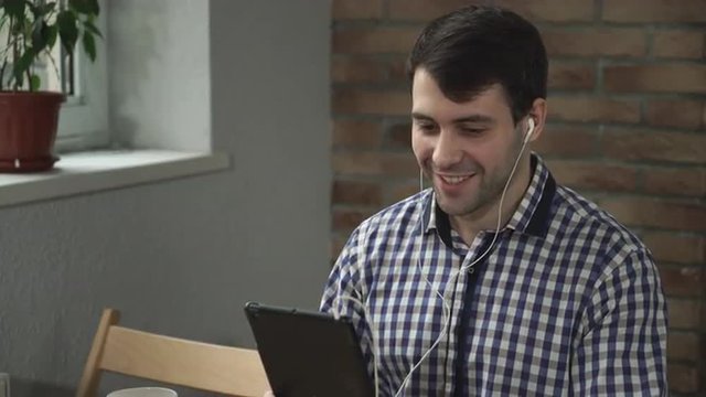 A man holding a tablet in the ears headphones, welcomed companion online.