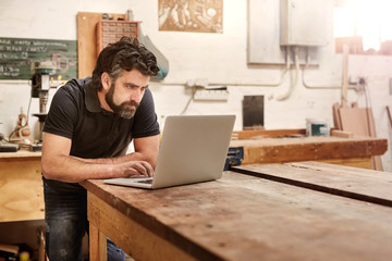 Small business owner in his workshop studio with laptop