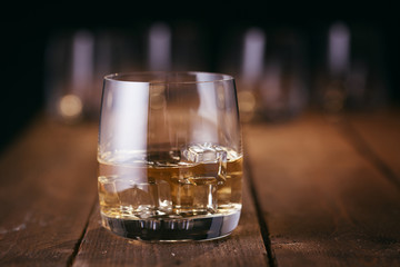 Glass of whiskey with ice cubes on wood table - obrazy, fototapety, plakaty