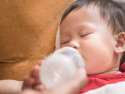 Asian Toddler Eating Bottle Of Milk Whilw Sleeping Indoor.