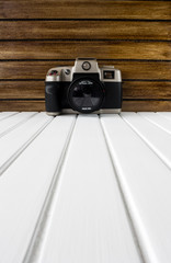 Vintage photo camera on white wooden base and brown wooden background 