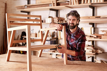 Artisan furniture designer sanding a chair in his workshop - obrazy, fototapety, plakaty