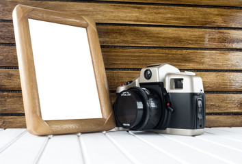 Vintage photo camera on white wooden base, brown wooden background and blank photo frame