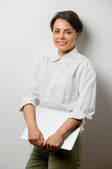 Attractive young woman standing against a wall holding a laptop