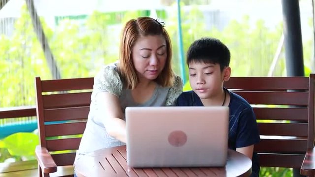 Young, happy asian mother with child using laptop on terrace