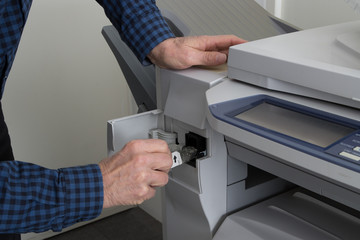 Man takes out black cartridge from white printer at work