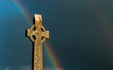Rainbow sky behind celtic cross gravestone at sunset