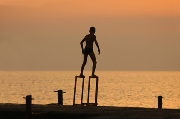 Fototapeta premium silouette of a boy ready to dive from pierce in front of brightl