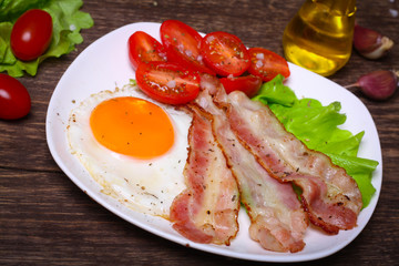 Hearty breakfast. Fried egg with bacon and tomatoes on a wooden background