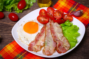 Hearty breakfast. Fried egg with bacon and tomatoes on a wooden background