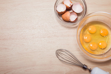 Broken eggs in a bowl with the blender and shell on the wooden background