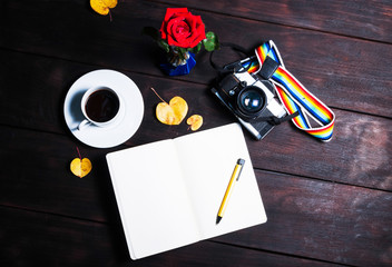 Retro camera, open memo book ,red rose and coffee cup on dard wo