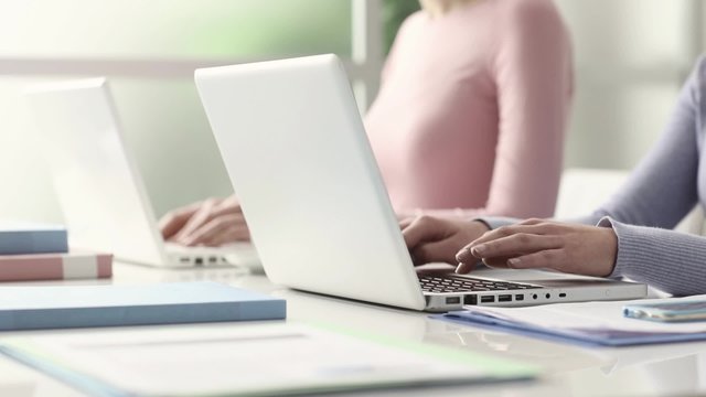 Young girls sitting at desk, studying and using a laptop, communication and learning concept, hands close up, seamless loop