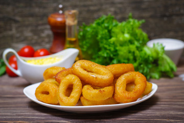 deep fried calamari with sauce and salad on a wooden background