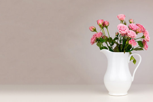 Pink flowers in white jug. Roses in jug.
