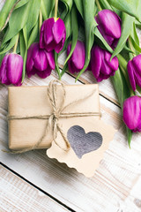 Gift box and tulips bouquet on white wooden background - retro style