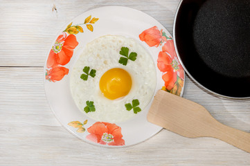 Fried eggs in a plate with a frying pan on a wooden background