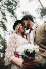 Romantic fairytale wedding couple kissing and embracing in pine forest near retro car.