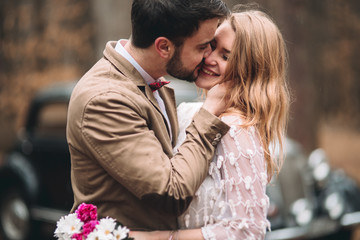 Fototapeta premium Romantic fairytale wedding couple kissing and embracing in pine forest near retro car.