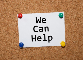 The phrase We Can Help  typed on a white piece of note paper and pinned to a cork notice board