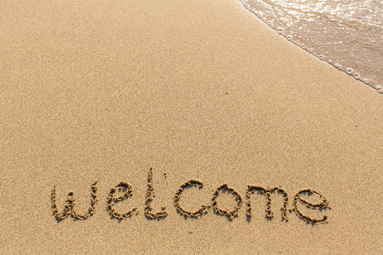 Welcome - word drawn on the sand beach with the soft wave.