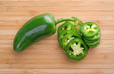 Jalapeno pepper plus slices on a wood cutting board.