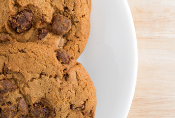Top close view of a plate of gourmet milk chocolate chip cookies on a wood table top.