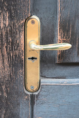 Golden door handle on old weathered wooden door