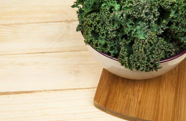 Fresh raw kale in ceramic bowl on the wooden table