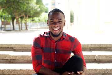 Fototapeta premium Smiling young african man sitting on steps outdoors