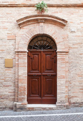 Fototapeta na wymiar Brown wooden door with arch in old stone wall