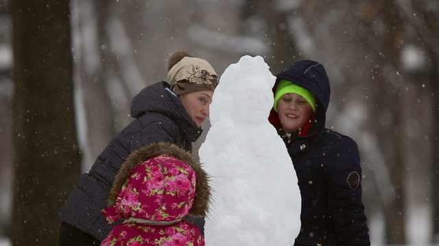 Happy family sculpts snowman out of snow in the park  during a snowfall
